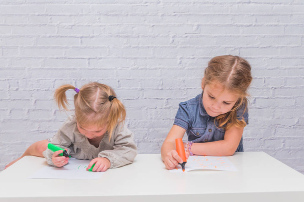 child, a girl at the table writes, draws on a piece of paper, against a white brick wall - Photo, Image