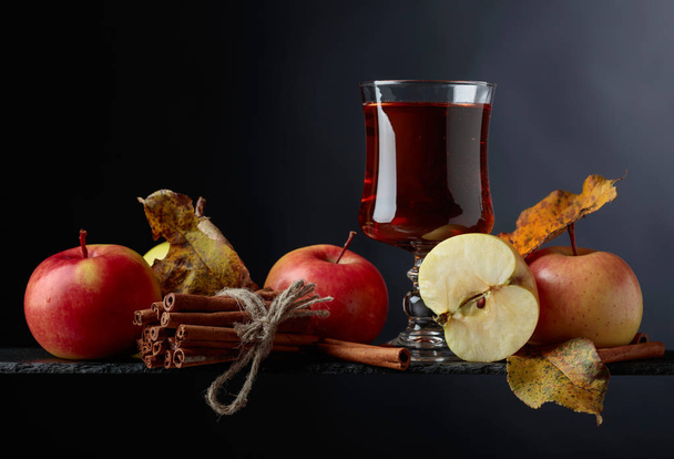 Apple juice  with juicy apples and cinnamon sticks on a black background, copy space. - Photo, Image