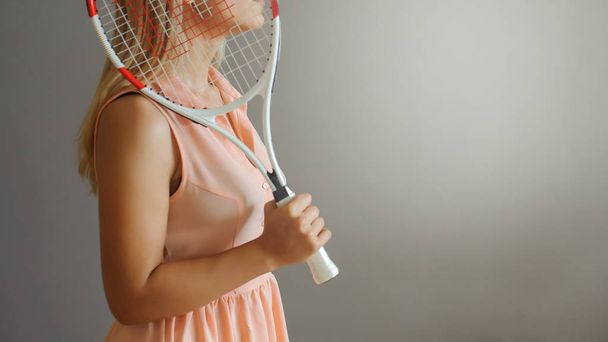 Una chica rubia bonita con paleta de tenis, vista cercana, fondo gris
 - Foto, imagen