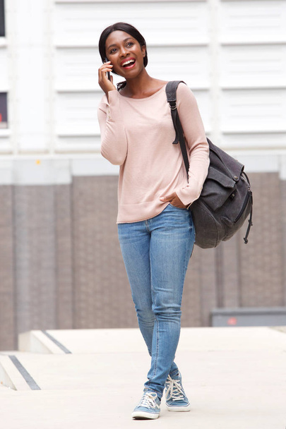 Full body portrait of happy young black woman walking and talking with mobile phone - Foto, Imagen