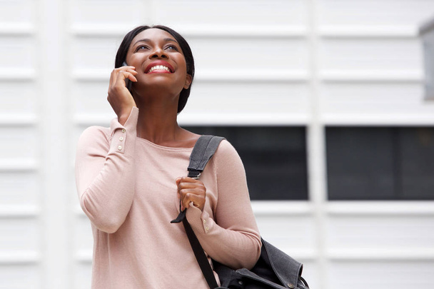 ウォーキングと携帯電話で話す笑顔の若いアフリカ系アメリカ人女性の肖像画  - 写真・画像