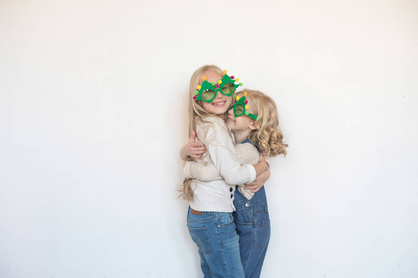 Two little girls hugging in funny glasses in the form of Christmas trees. - Fotografie, Obrázek