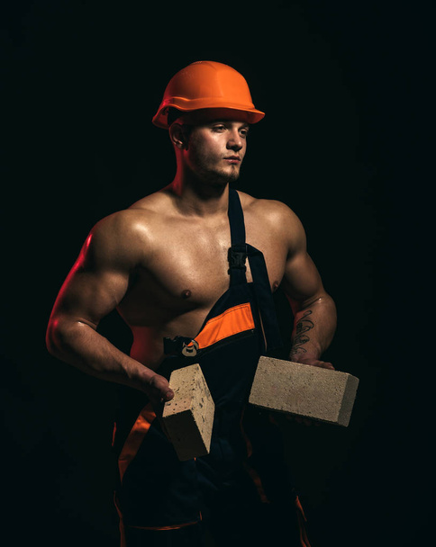 We are building dreams. Bricklayer worker. Construction worker or builder at work at building site. Man worker hold bricks in muscular hands. Muscular man does masonry work - Photo, Image
