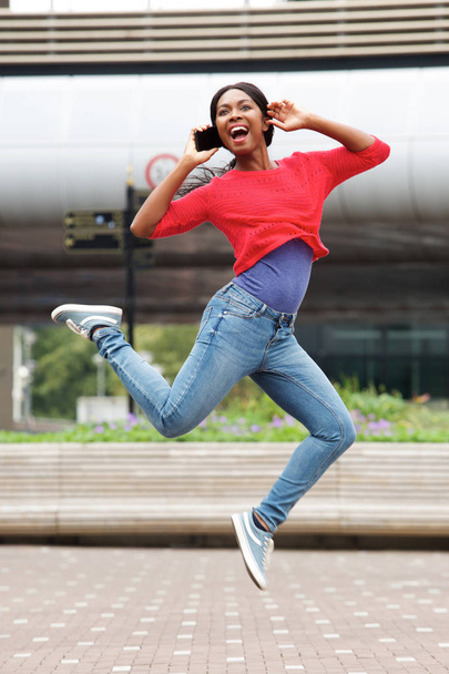 Portrait complet d'une jeune femme noire joyeuse sautant dans les airs avec un téléphone portable
 - Photo, image