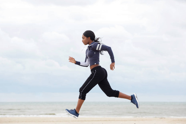 Full body side portrait of african american woman running by the beach - Foto, Imagen