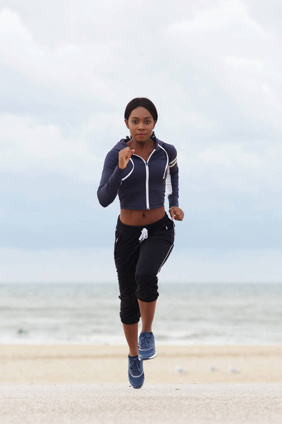 Retrato frontal de corpo inteiro de uma jovem negra correndo na praia
  - Foto, Imagem
