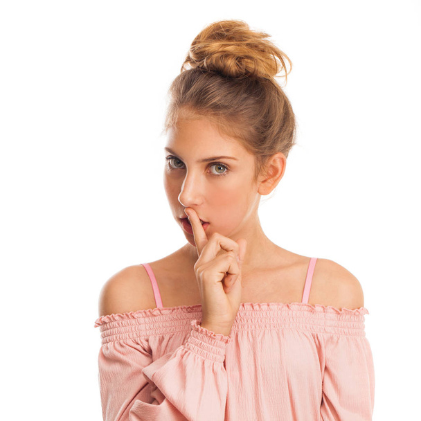 Blonde little girl requires silence. Young beautiful teenager has put forefinger to lips as sign of silence, isolated on white - Photo, image