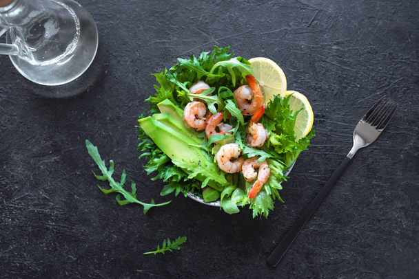 Avocado Shrimp Salad on black stone background, copy space. Healthy diet green salad with Shrimps (prawns), avocado and arugula. - Photo, Image