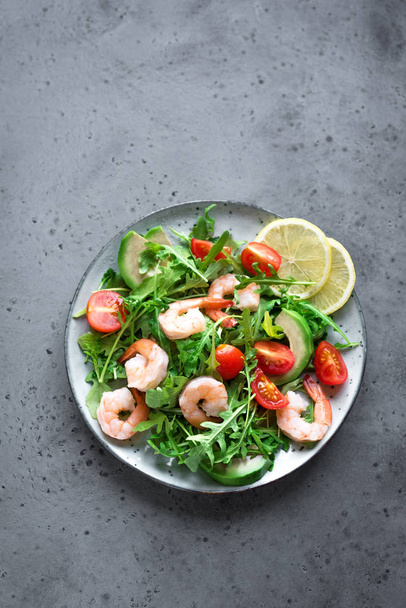 Avocado Shrimp Salad with Arugula and Tomatoes on grey stone background, copy space, top view. Healthy diet green salad with Shrimps (prawns), avocado, cherry tomato and arugula. - Foto, afbeelding