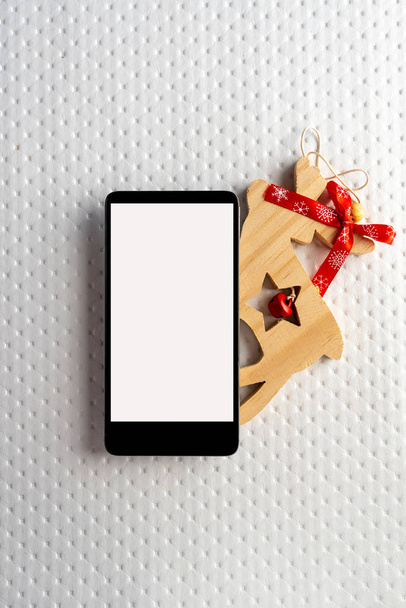 Teléfono móvil vacío de Navidad sobre fondo rojo, planificación de vacaciones y renos de madera sobre fondo blanco
 - Foto, Imagen