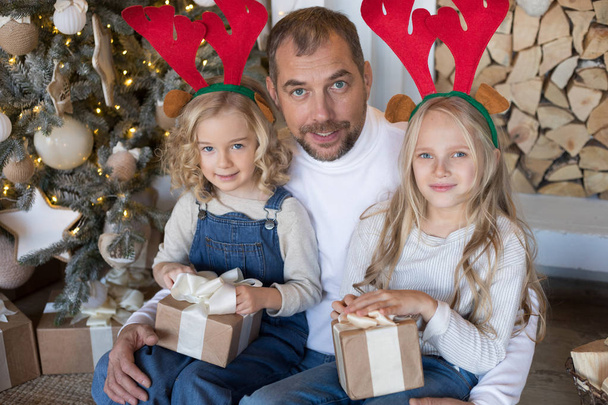 Papà è seduto con due figlie vicino all'albero di Natale
. - Foto, immagini