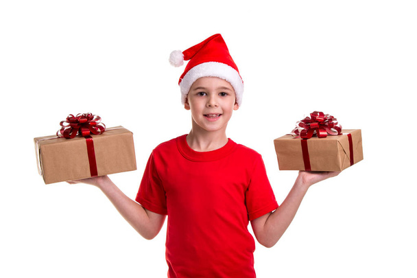 Szép boldog fiú, santa kalap a fején, két ajándék doboz a kezében, nézett egyenesen a kamera. Koncepció: karácsonyi vagy boldog újévi ünnep - Fotó, kép