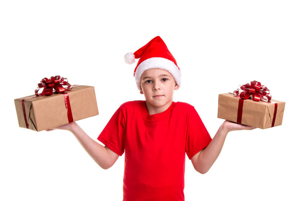Handsome serious boy, santa hat on his head, with two gift boxes on the hands, puzzled to make a choise among two gifts. Concept: christmas or Happy New Year holiday - Foto, immagini