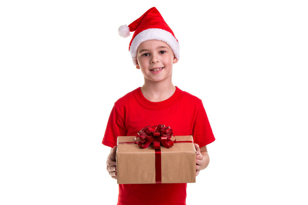 Guapo niño feliz, sombrero de santa en la cabeza, con la caja de regalo en las manos. Concepto: Navidad o Feliz Año Nuevo
 - Foto, Imagen