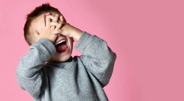 Baby boy kid covering close his eyes with hands and palms screaming laughing  over pink - Fotoğraf, Görsel