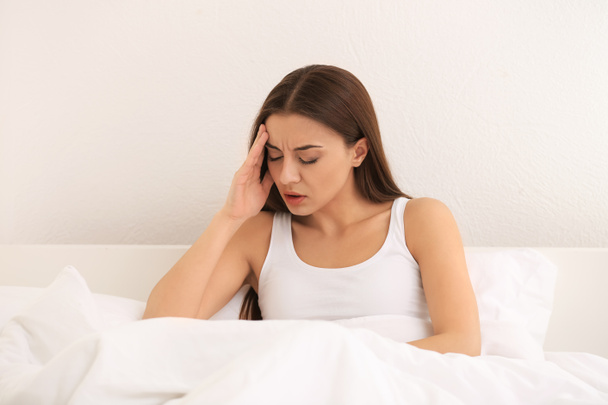 Woman suffering from headache in bedroom - Foto, afbeelding
