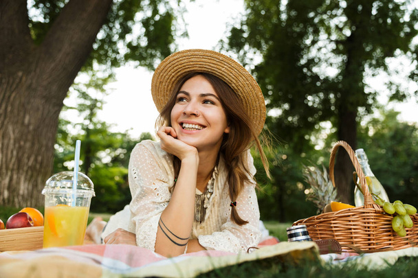 Happy young girl in summer hat having a picnic at the park, laying on a grass - Foto, imagen