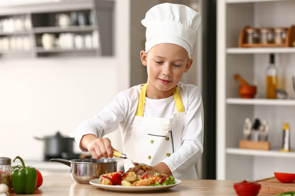 Cute little chef dressing tasty dish in kitchen - Фото, изображение