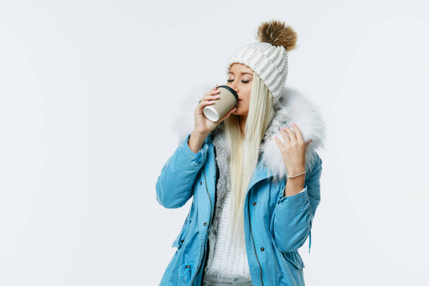 Woman in blue coat with fur holding a cup of coffee at the white background. Coffee to go concept - 写真・画像