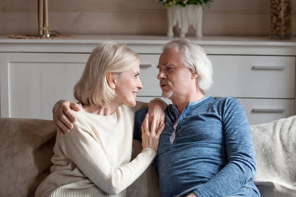 Happy aged couple cuddle on couch having talk - Photo, Image