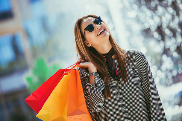 Kaunis tyttö aurinkolasit tilalla ostoskassit ja hymyillen kävellessään kadulla
 - Valokuva, kuva