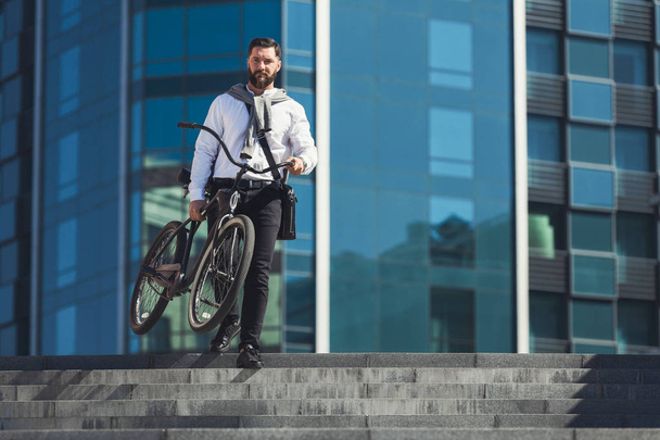 Brodaty biznesmen, niosąc jego rower na schodach - Zdjęcie, obraz