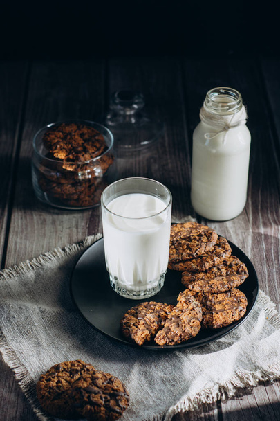 Glass with fresh milk and homemade chocolate chips cookies over a wooden table.  - Фото, изображение