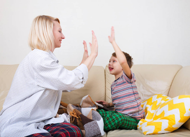 High five between son and mom. Happy mother and son playing games at home sitting on the bed, clapping hands together - Foto, imagen