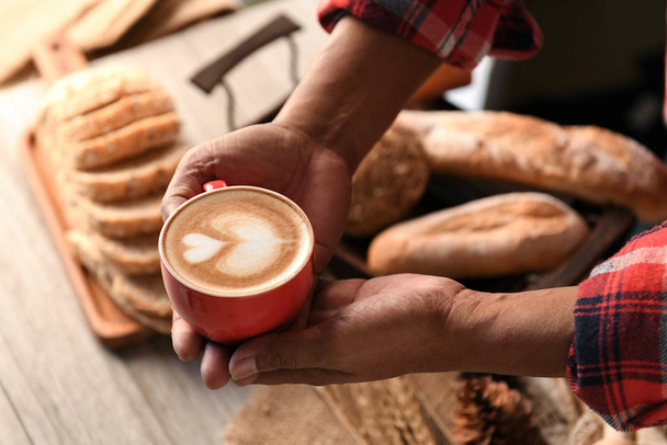 Heart latte coffee in barista hand with bread on wooden tray. - Valokuva, kuva