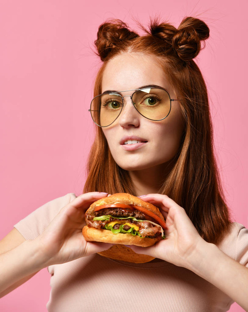 Stylish and young girl in sunglasses holding burger on pink background. - Foto, imagen