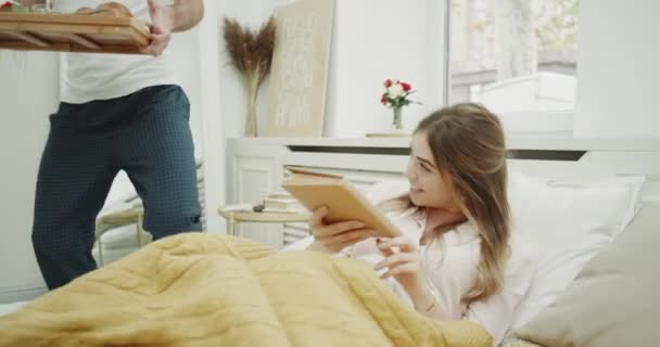 In the morning lady reading a book and waiting for her breakfast in bed from her boyfriend , they happy starting take the and feeling happy. shot on red epic. - Materiaali, video