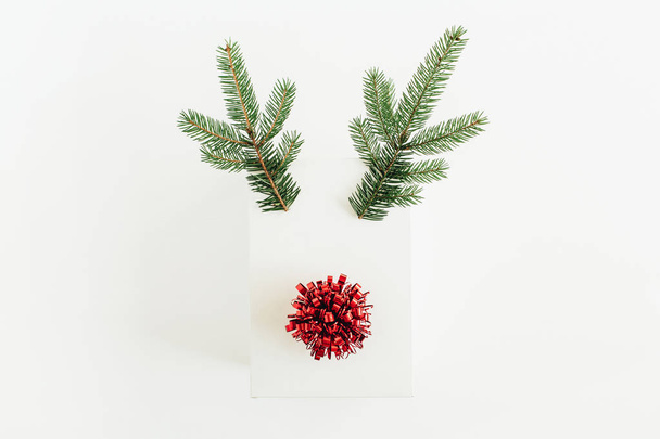 Christmas, New Year minimal concept. Christmas deer symbol made of white gift box, fir branches and red pompon isolated on white background. Flat lay, top view. - Photo, Image