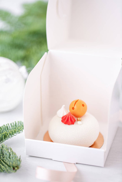 Mini mousse gebak dessert bedekt met witte velours. Individueel verpakt in witte doos. De takken van een spar op de achtergrond bokeh. Moderne Europese taart. Franse keuken. Kerstmis. Sneeuwvlok - Foto, afbeelding