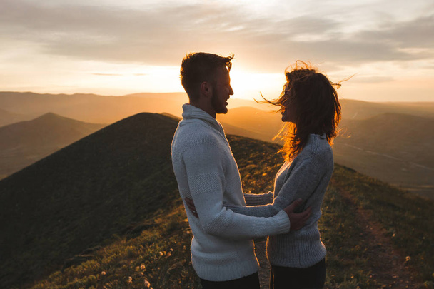 Счастливая пара обнимается и целуется на закате с потрясающим видом на горы. Теплый вечерний солнечный свет
 - Фото, изображение