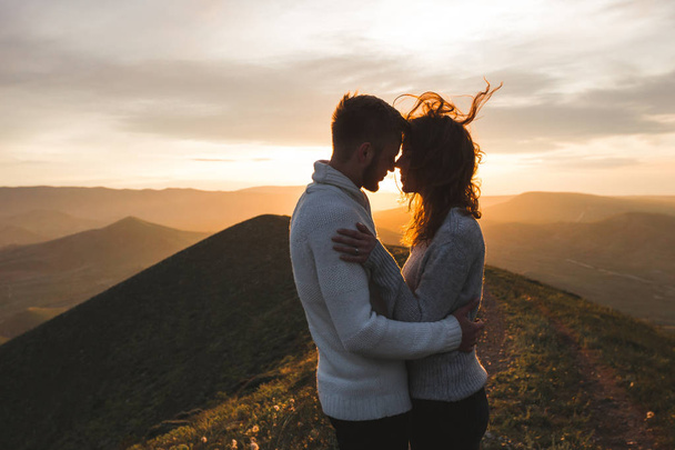 Happy couple hugging and kissing at sunset witn amazing mountain view. Warm evening sun light - Fotó, kép