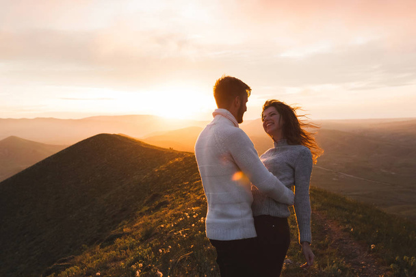 Ευτυχισμένο ζευγάρι αγκάλιασμα και το φίλημα στο ηλιοβασίλεμα witn καταπληκτική θέα στο βουνό. Το βράδυ ζεστό φως του ήλιου - Φωτογραφία, εικόνα