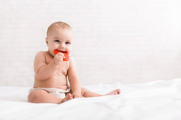 Νεογέννητο μωρό δαγκώνει κόκκινο οδοντοφυΐας στο κρεβάτι - Φωτογραφία, εικόνα