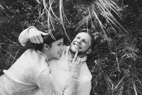 Happy young loving couple lying in feather grass, laughing and hugging, view from above. Black and white style - Photo, Image