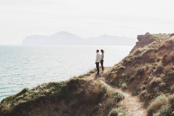 Young couple walking on nordic sea coast with mountain view in spring, casual style clothing sweaters and jeans - Foto, immagini