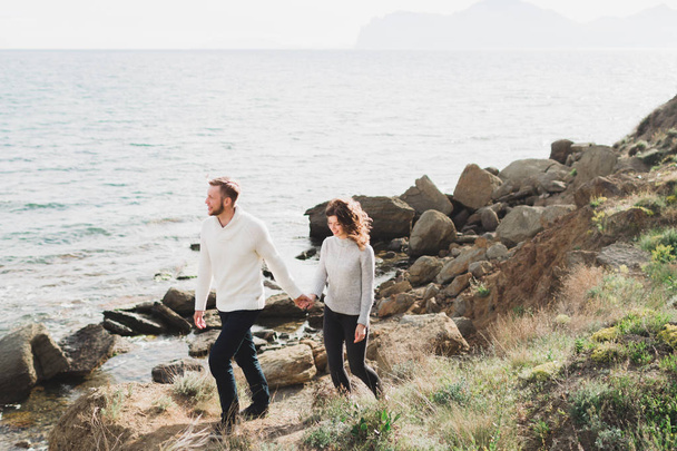 Fiatal pár, tavaszi stílusú alkalmi ruhák pulóverek és a farmer séta Északi-tenger partján, kilátással a hegyre - Fotó, kép