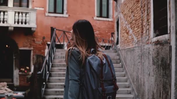 Camera follows beautiful travel blogger woman walking with camera on stairs in Venice street, taking a photo slow motion - Filmati, video