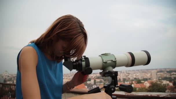 Młoda kobieta, patrząc na panoramę miasta, za pomocą teleskopu - Materiał filmowy, wideo
