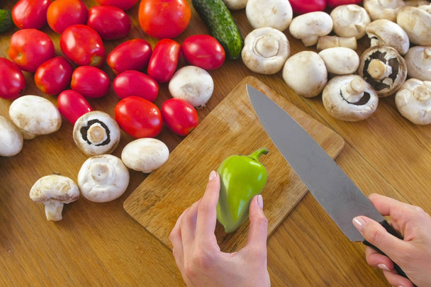 Womans hands peel green pepper on wooden board on kitchen table with vegetables. - Fotó, kép