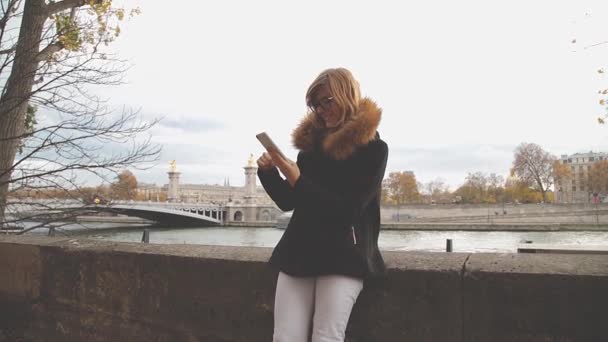 Fiatal nő használ smartphone kültéri, híd a folyón, a háttér. - Felvétel, videó