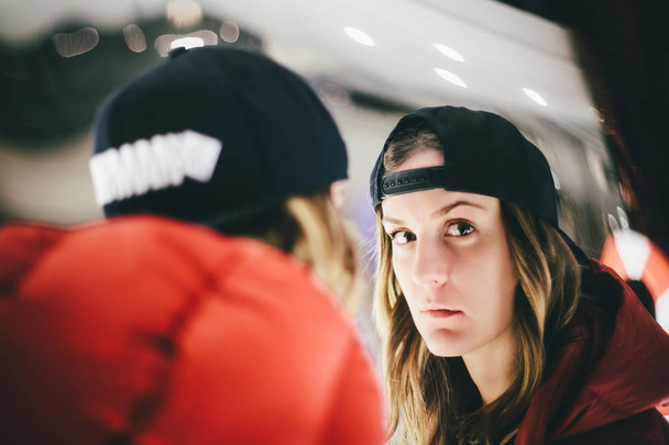 Trendy charming girl in red jacket wearing stylish cap looking at false glass with pensive face - Foto, imagen