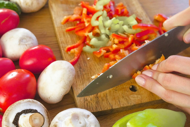 Womans hands peel green pepper on wooden board on kitchen table with vegetables. - Photo, Image