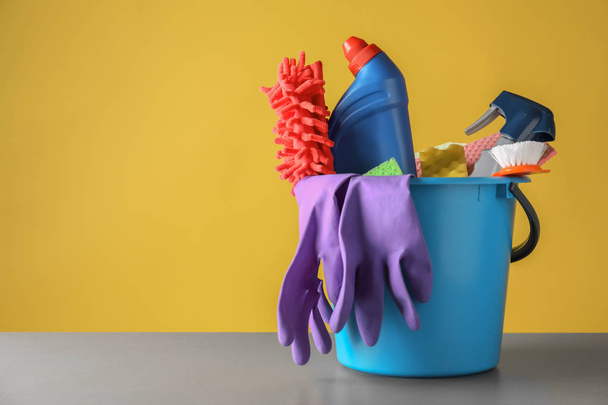 Ведро с чистящими средствами на столе на цветном фоне
 - Фото, изображение