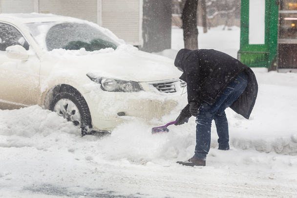 車の街に雪のドリフトをブロックします。大雪、吹雪と嵐の中にブラシで雪から車の掃除人。冬の天気予報. - 写真・画像