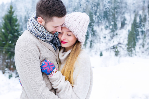 Nahaufnahme eines Liebespaares in Pullovern, die sich vor dem Hintergrund der Winterberge umarmen - Foto, Bild