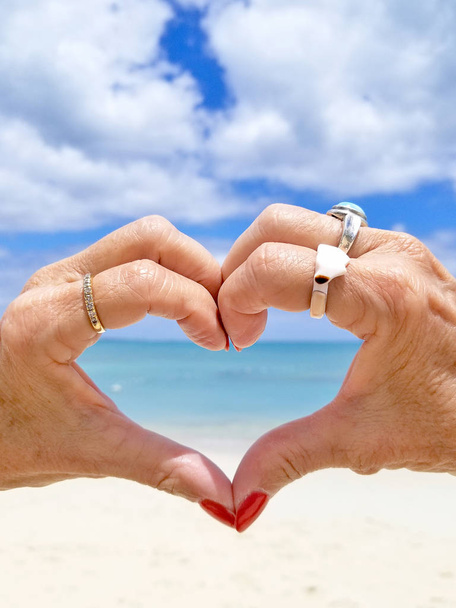 пара рук, використовуючи пальці, щоб сформувати серце з видом на тропічний пляж і океан
 - Фото, зображення